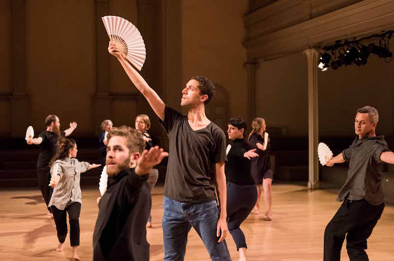 A cluster of dancers move independently with fans in their palms